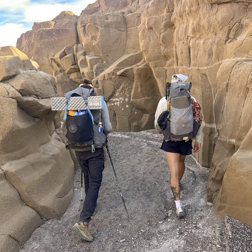 Hikers on a gravelly trail between rock walls.