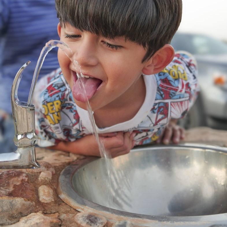 A boy drinking water from a fountain.