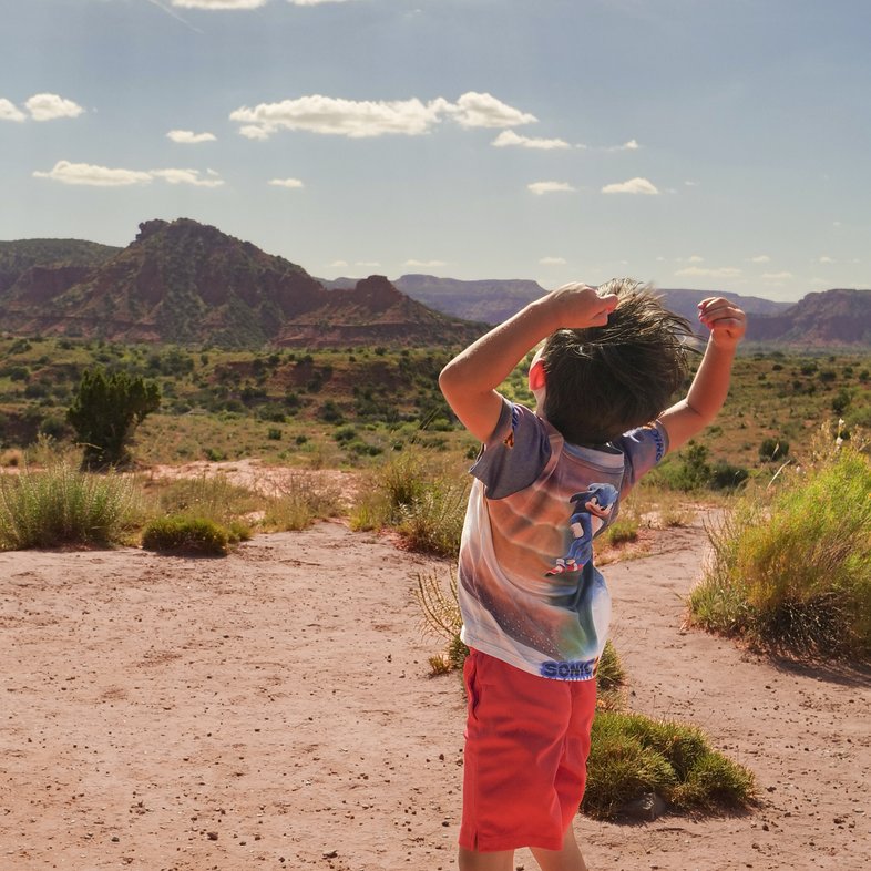 A boy with hands raised over his head with an arched back in Cap Rock Canyons