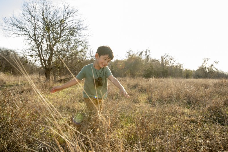 A boy walking through a grassy field.