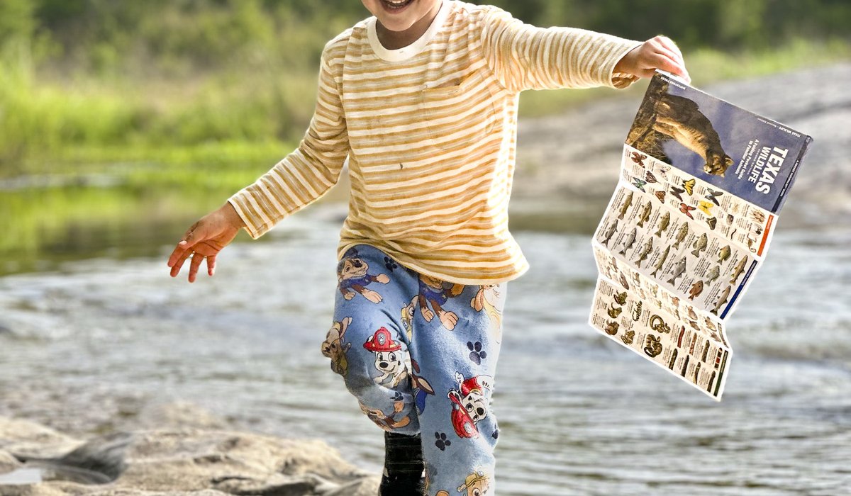 A boy running along a rocky shore holding a Texas Dinosaur guide
