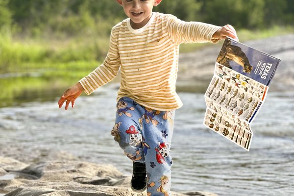 A boy running along a rocky shore holding a Texas Dinosaur guide