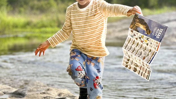 A boy running along a rocky shore holding a Texas Dinosaur guide