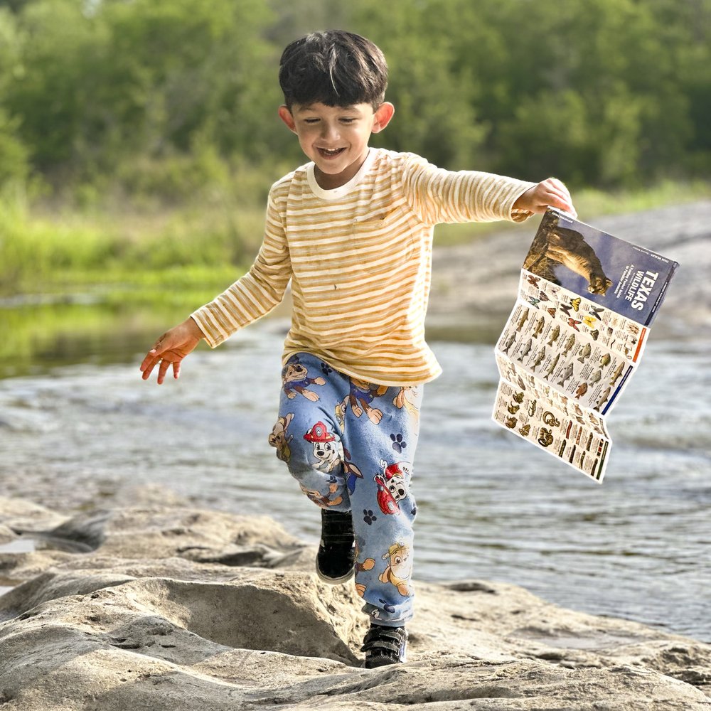 A boy running along a rocky shore holding a Texas Dinosaur guide