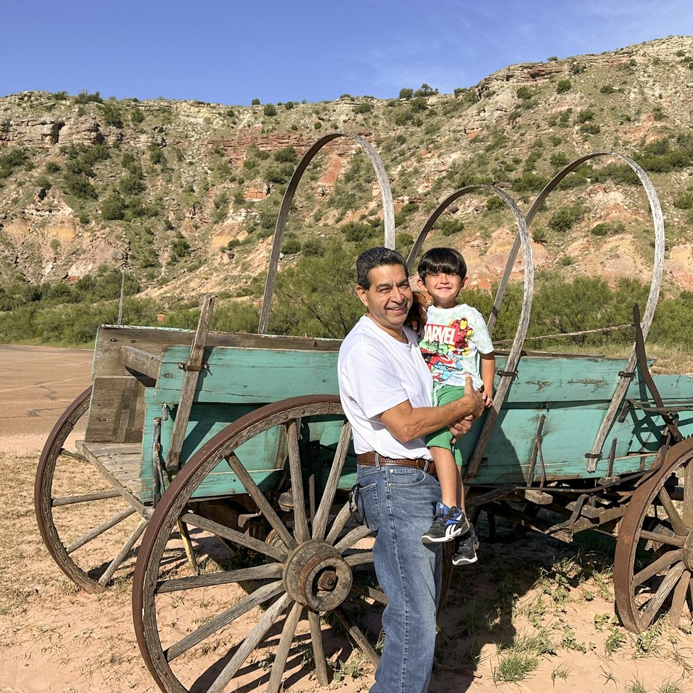 Man holding a child in a canyon with a old covered wagon in the background