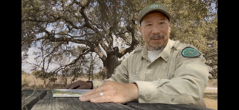 A park interpreter sitting a a picnic table with a book being photographed.