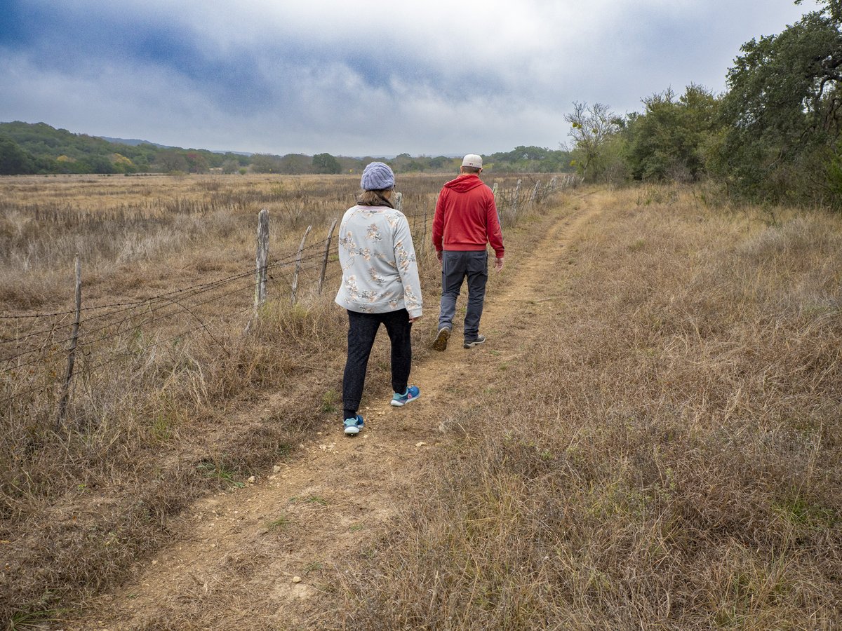 People walking a trail near a fence line.