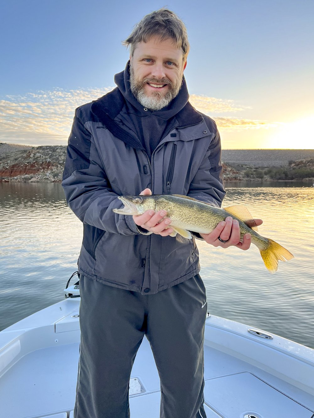 A man poses with a walleye fish on a boat on the lake