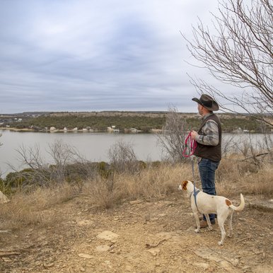 A man in a brown cowboy hat poses at a scenic overlook with his white and brown dog