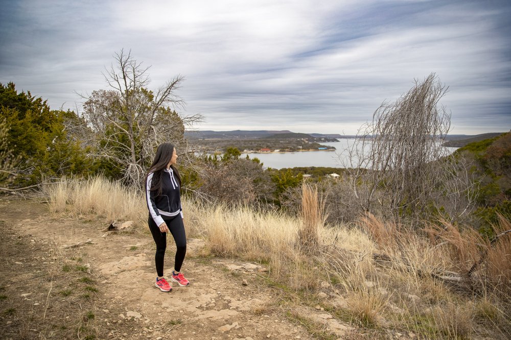 A woman in black leggings hikes on a trail over looking the lake