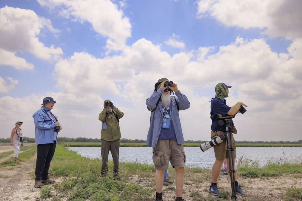 A group of people standing next to a pond look through binoculars
