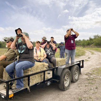 A group of people look through binoculars while sitting on a trailer with hay bails