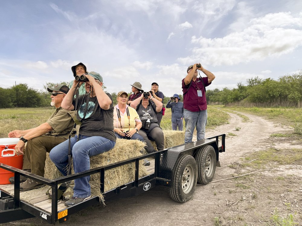 A group of people look through binoculars while sitting on a trailer with hay bails