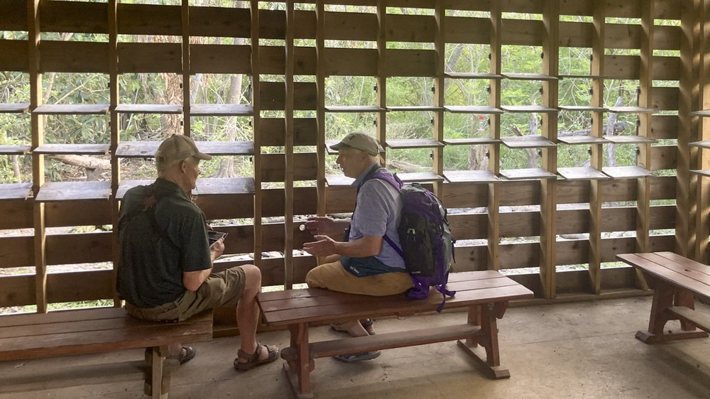 Two men wearing hats sit inside a bird blind