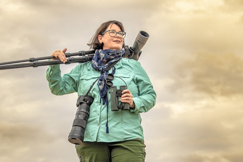 Jennifer Bristol holding binocular on a stand at sunrise in a grassy field.