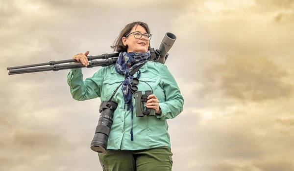 Jennifer Bristol holding binocular on a stand at sunrise in a grassy field.
