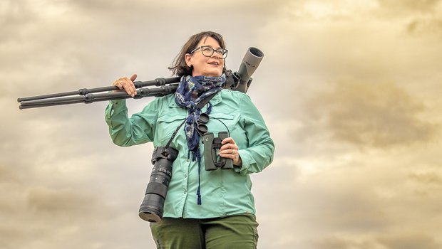 Jennifer Bristol holding binocular on a stand at sunrise in a grassy field.