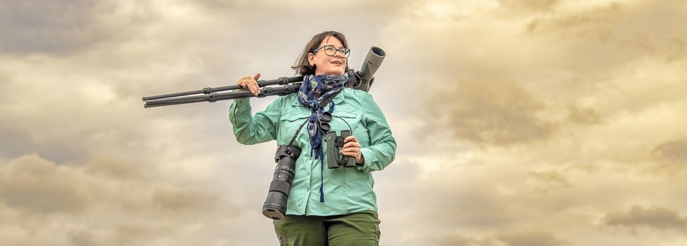 Jennifer Bristol holding binocular on a stand at sunrise in a grassy field.