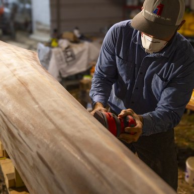Canoe builder sanding the hull of his cedar strip racing canoe in workshop