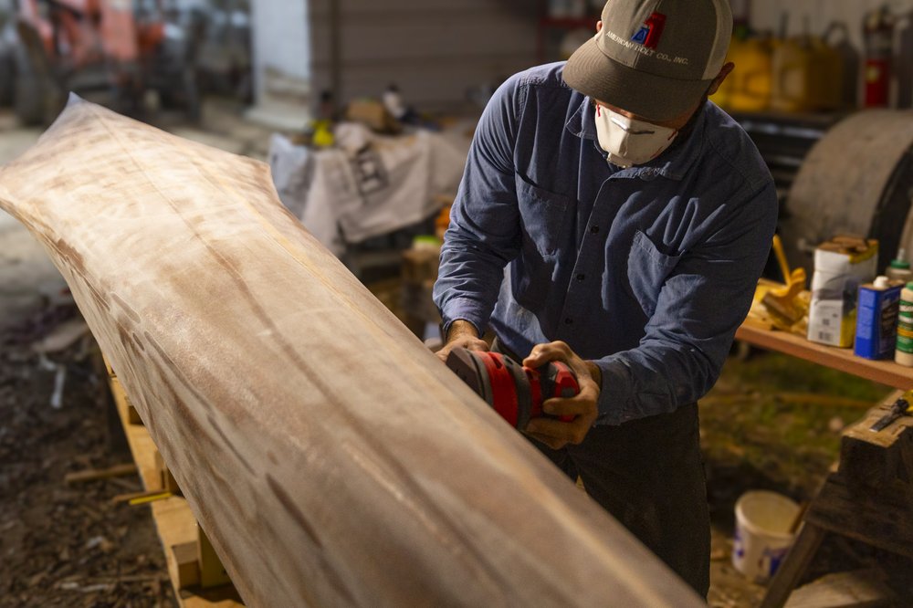 Canoe builder sanding the hull of his cedar strip racing canoe in workshop
