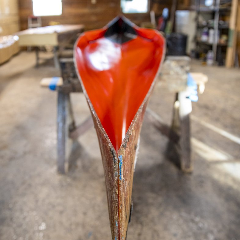 Front view of racing canoe with red epoxy drying in workshop