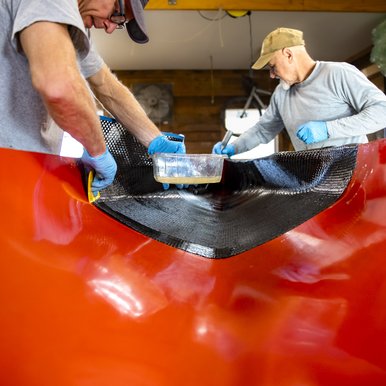 Two builders putting on epoxy to racing canoe in workshop