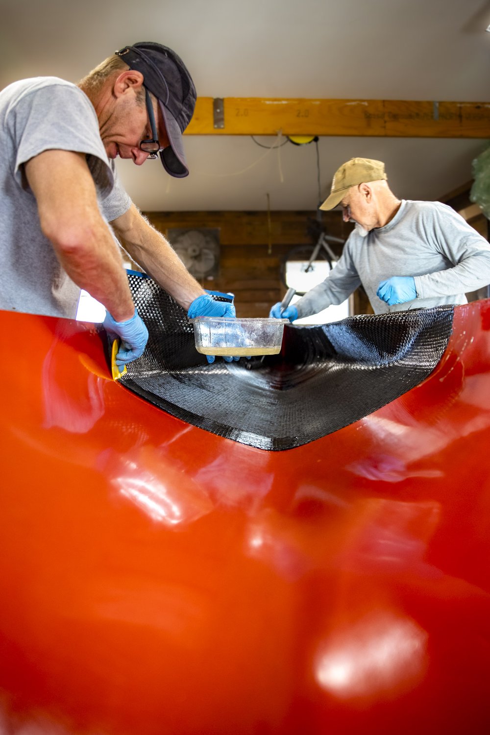 Two builders putting on epoxy to racing canoe in workshop