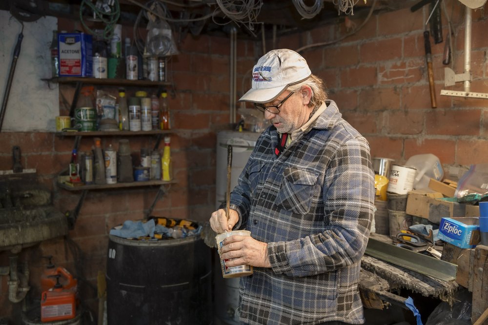 Canoe builder stirring epoxy in a can in front of his workbench lined with canoe building equipment