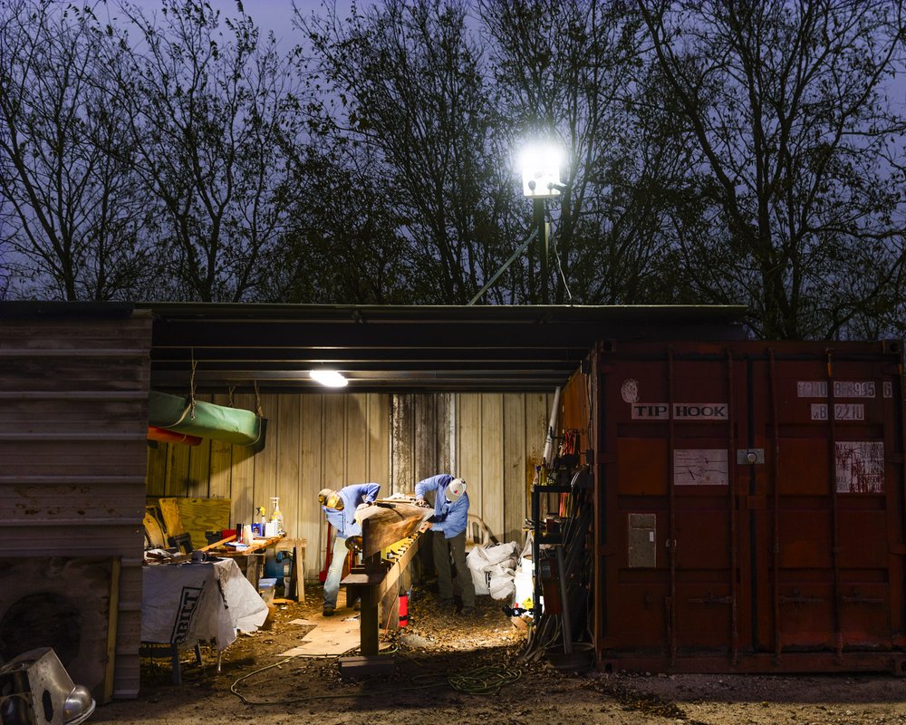 Two paddlers work on a racing canoe in Travis County shed at nighttime