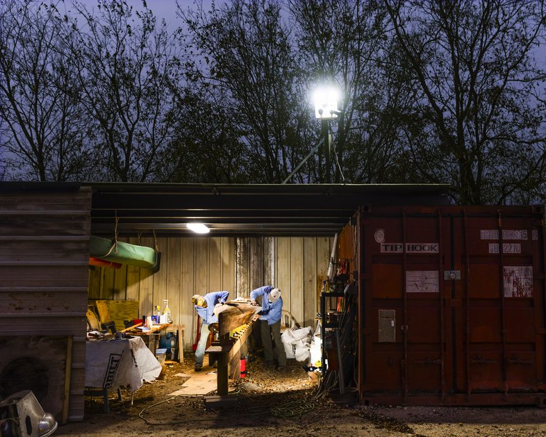Two paddlers work on a racing canoe in Travis County shed at nighttime