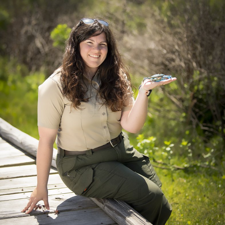 Portrait of Regina Lillibridge sitting on wooden trail holding a blue crab