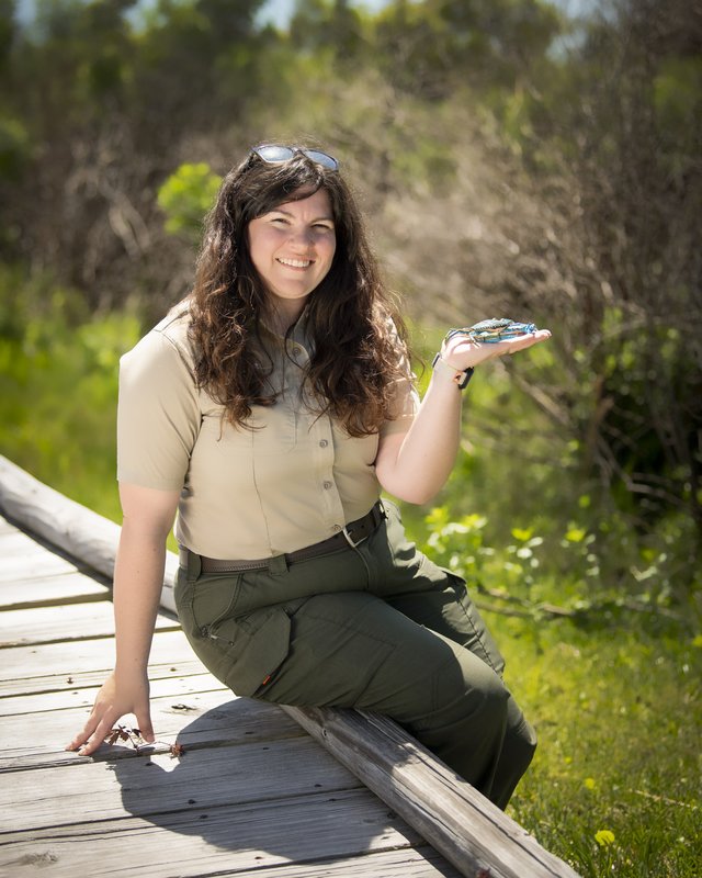 Portrait of Regina Lillibridge sitting on wooden trail holding a blue crab