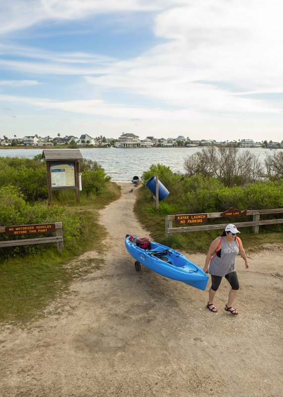 Female paddler is rolling a blue kayak away from launching area off the Galveston Bay