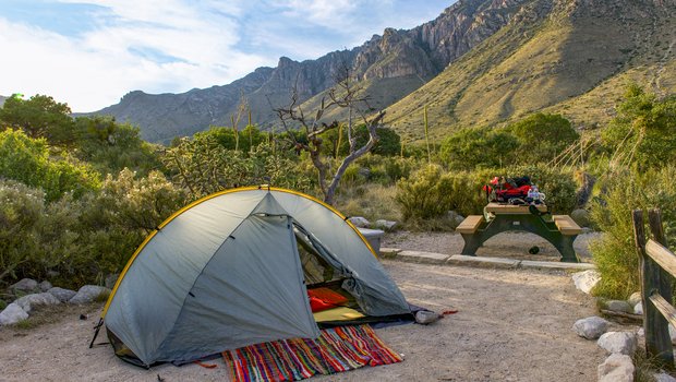 Tent with blanket and sleeping mattress erected at campsite with Guadalupe Mountains in the background