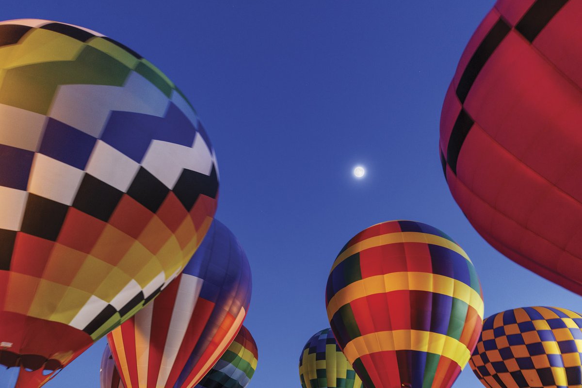 Hot air balloons floating just above the ground with full moon in background at night