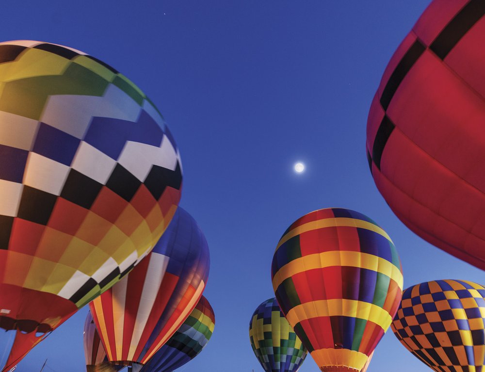 Hot air balloons floating just above the ground with full moon in background at night