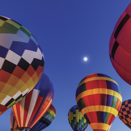 Hot air balloons floating just above the ground with full moon in background at night