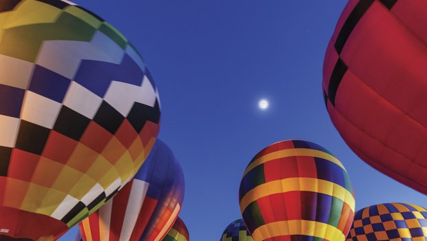 Hot air balloons floating just above the ground with full moon in background at night