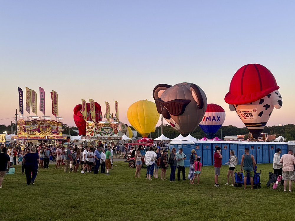 Festival fairgrounds with food stands, games and character hot air balloons make the sky colorful at sunset