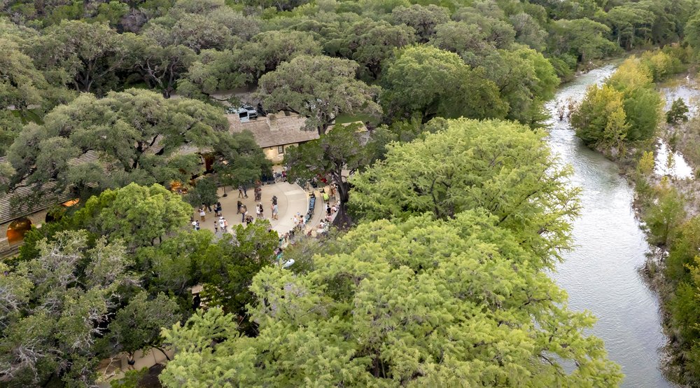 People gathering a a pavillion surrounded by trees.