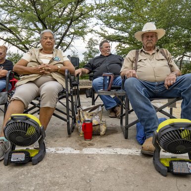 People sitting in chairs outdoors with fans on the ground pointing at them.