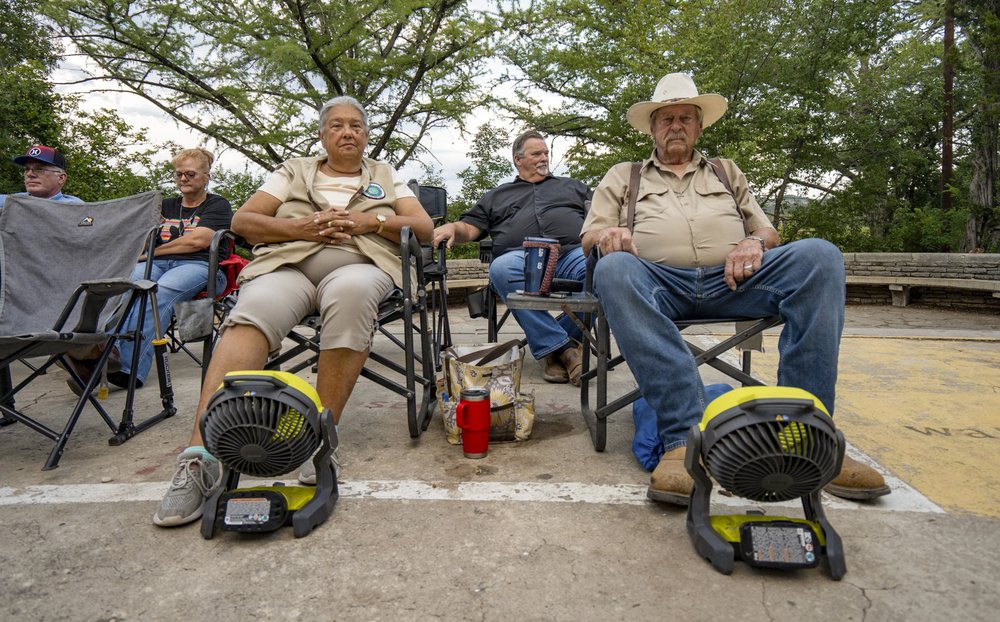 People sitting in chairs outdoors with fans on the ground pointing at them.