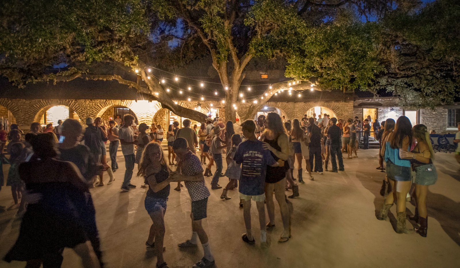 People dancing at night with string lights above.