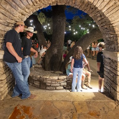 People gathered in an stone archway with people on the other side gathering for a dance.