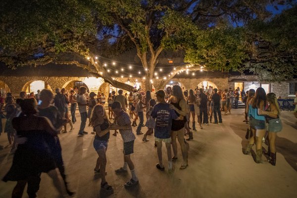 People dancing at night with string lights above.