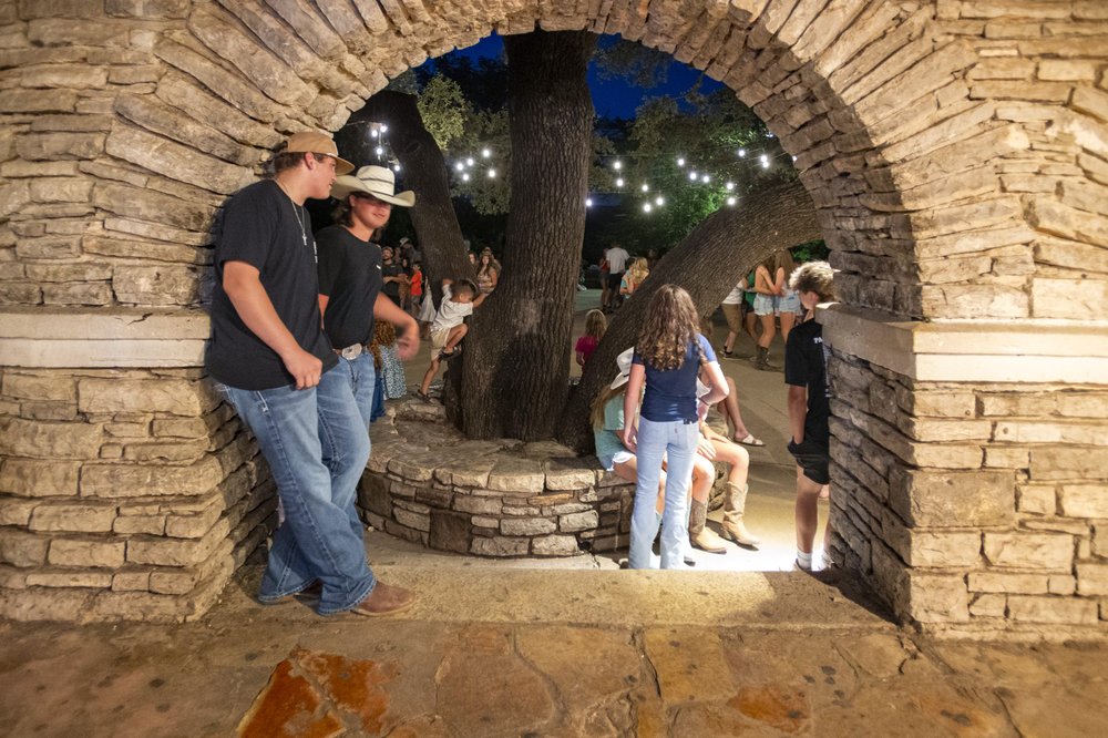 People gathered in an stone archway with people on the other side gathering for a dance.