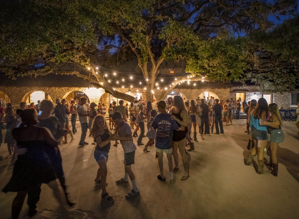 People dancing at night with string lights above.