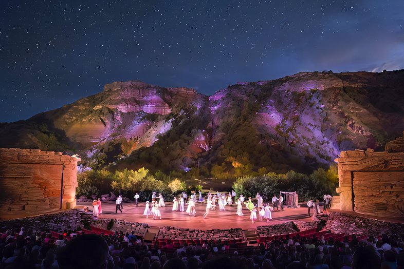 People performing on a stage with a large hill behind in the background.