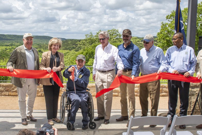 People holding a red ribbon that is being cut.