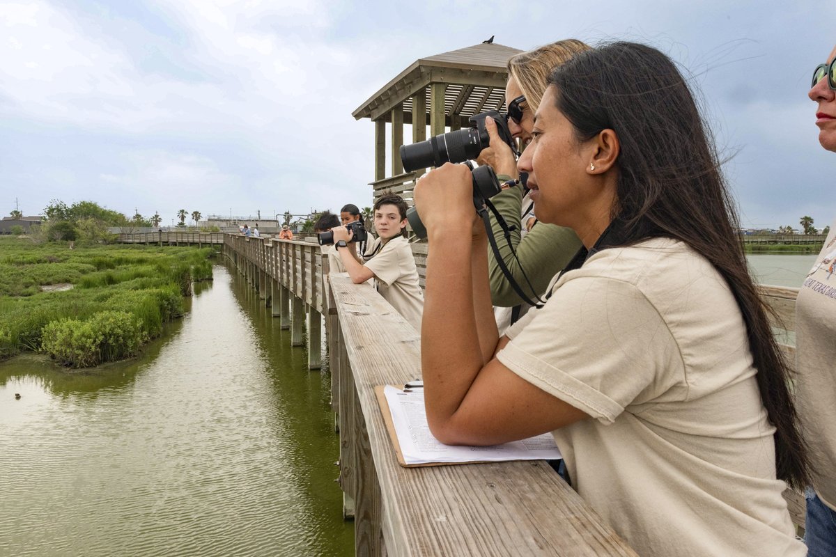 Children on a wooden bridge trail with the person in the foreground using binoculars.